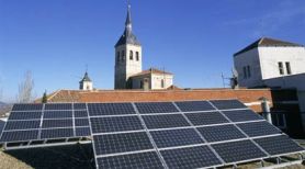 Instalación de placas solares en un pueblo donde se ve la torre de la iglesia sobre cielo azul