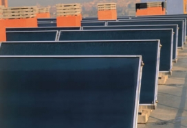 Front view of a solar power system comprising eight rows of panel on the roof of a building with red chimneys