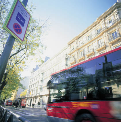 Ahorro y eficiencia energética: transporte. Vista de un autobús urbano en movimiento junto a una señal de prohibido estacionar sobre el fondo de altos edificios residenciales