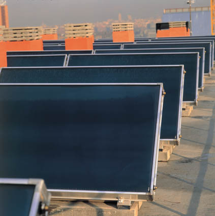 Vista frontal de una instalación de placas solares de ocho filas en la azotea de un edificio con chimeneas rojas