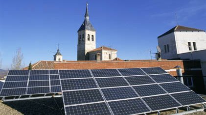 Instalación de placas solares en un pueblo donde se ve la torre de la iglesia sobre cielo azul