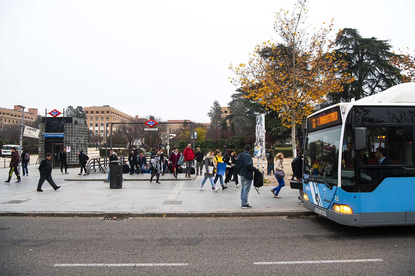Estudiantes caminando al lado de una estación de metro y un autobús urbano