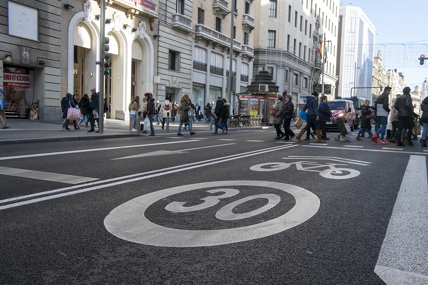 Peatones cruzando un semáforo en la calle Gran Vía de Madrid. En la calzada destaca señalizado la limitación de velocidad a 30Km hora y el carril bici